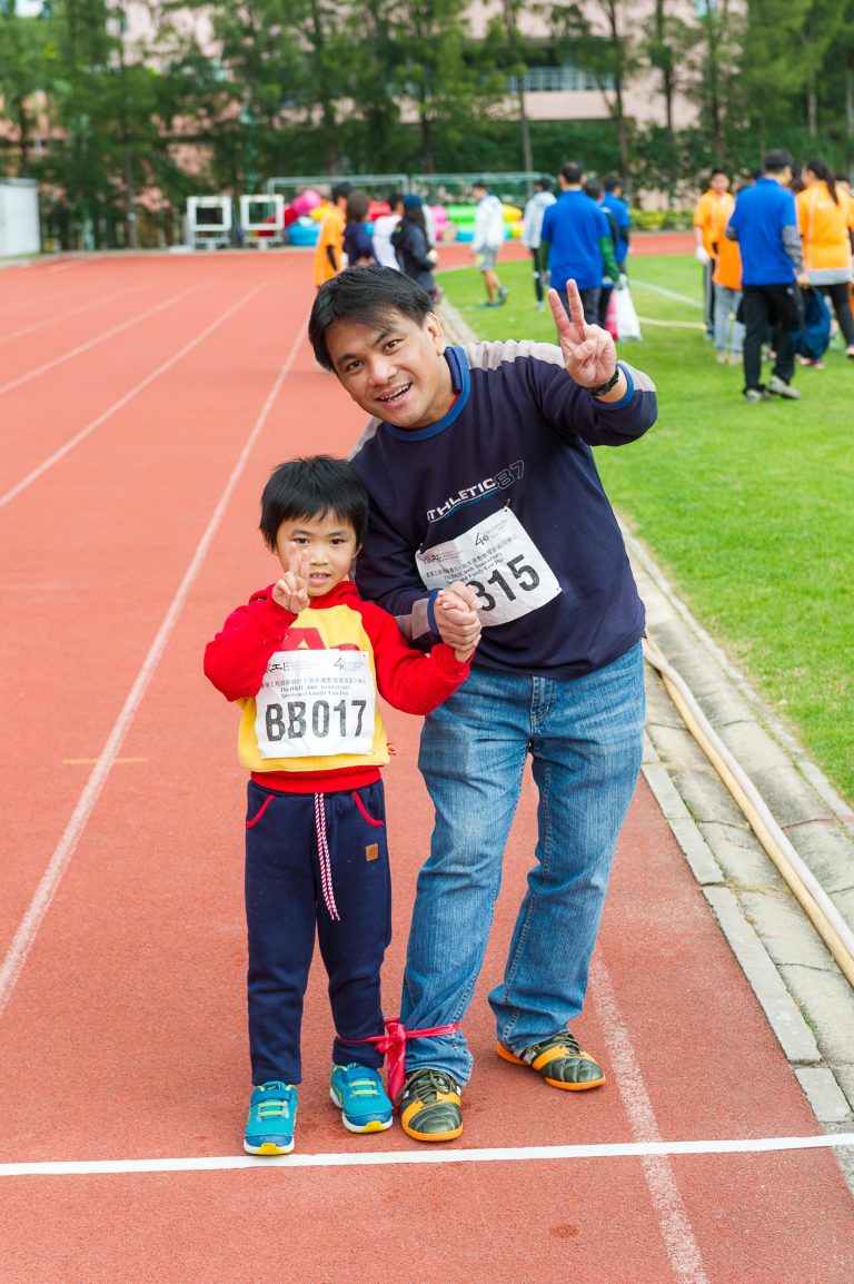 Man and child posing on track, both holding peace sign, wearing race bibs